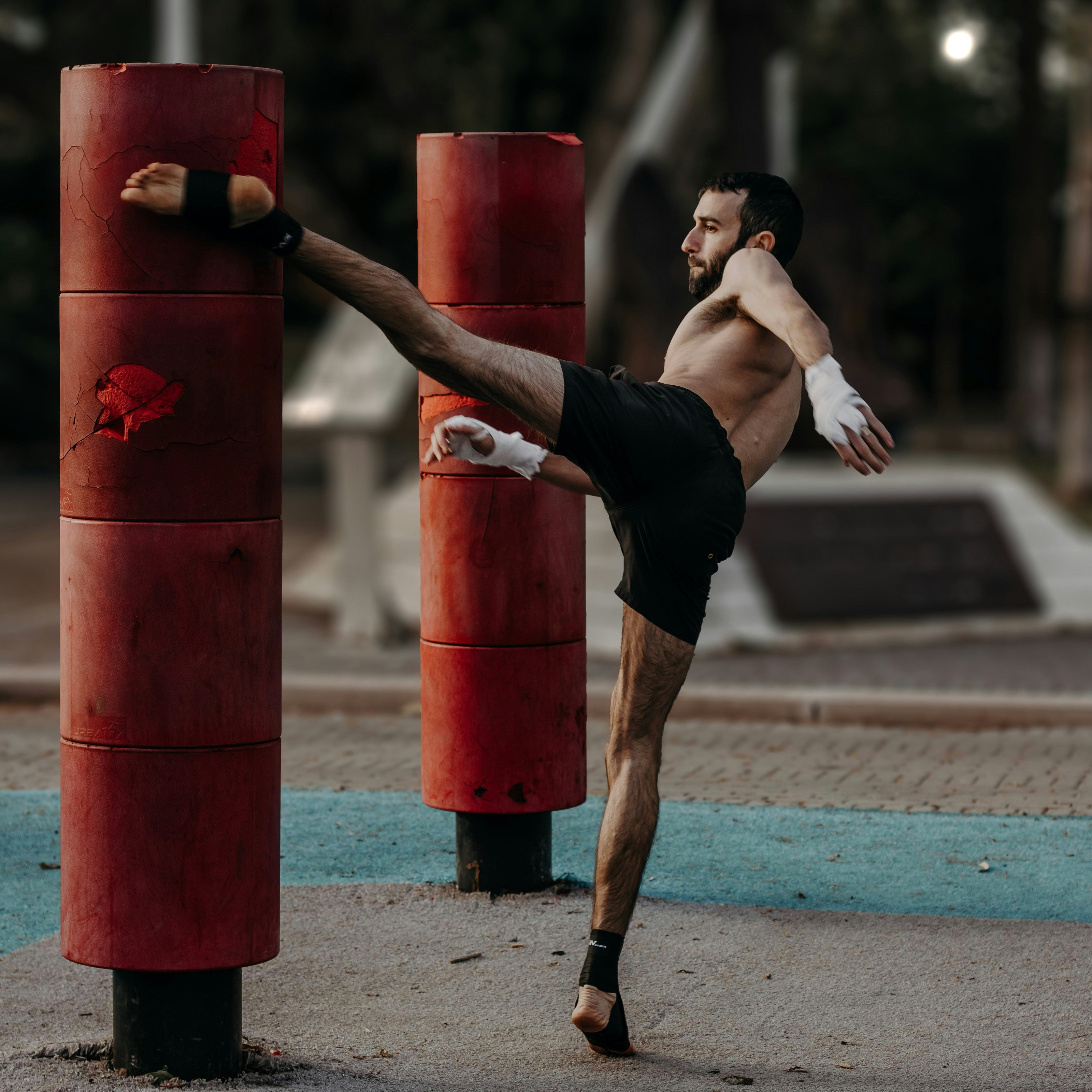 Man practicing martial arts on red punching bags outdoors